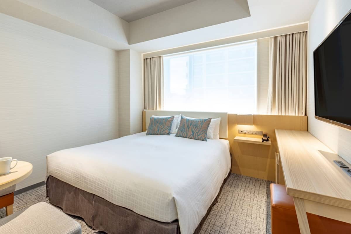 Une chambre d’hôtel avec un grand lit, une table de chevet, une télévision et une fenêtre avec des rideaux.