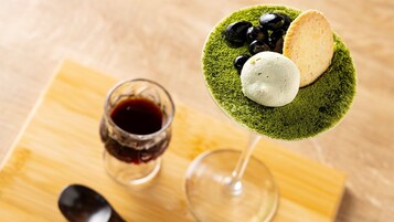 Un verre à martini avec un bord vert, une boule de crème glacée, des olives noires et une tranche de pain sur une planche en bois.