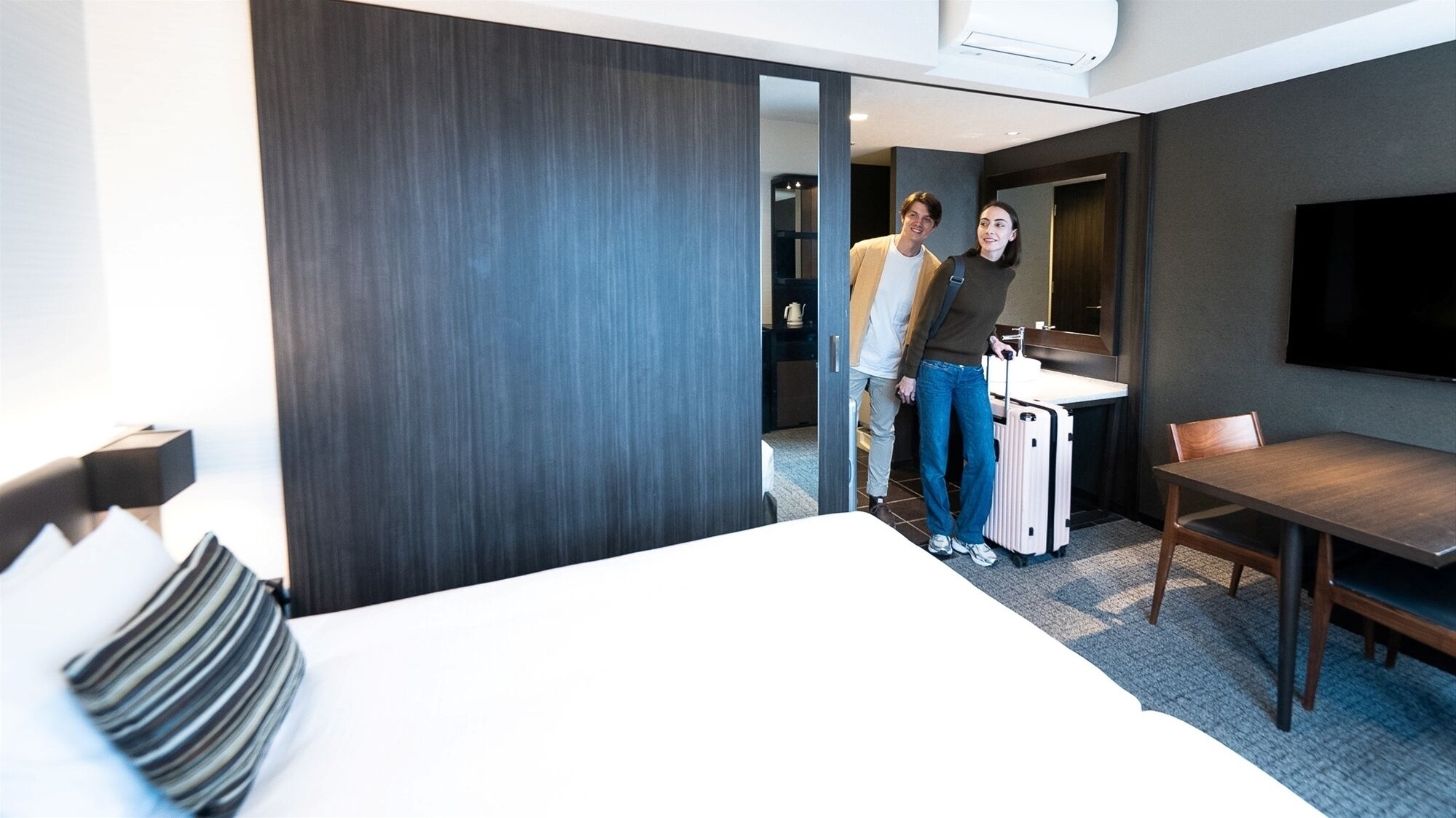 Habitación de hotel con cama, escritorio, silla, televisor y zona de baño.