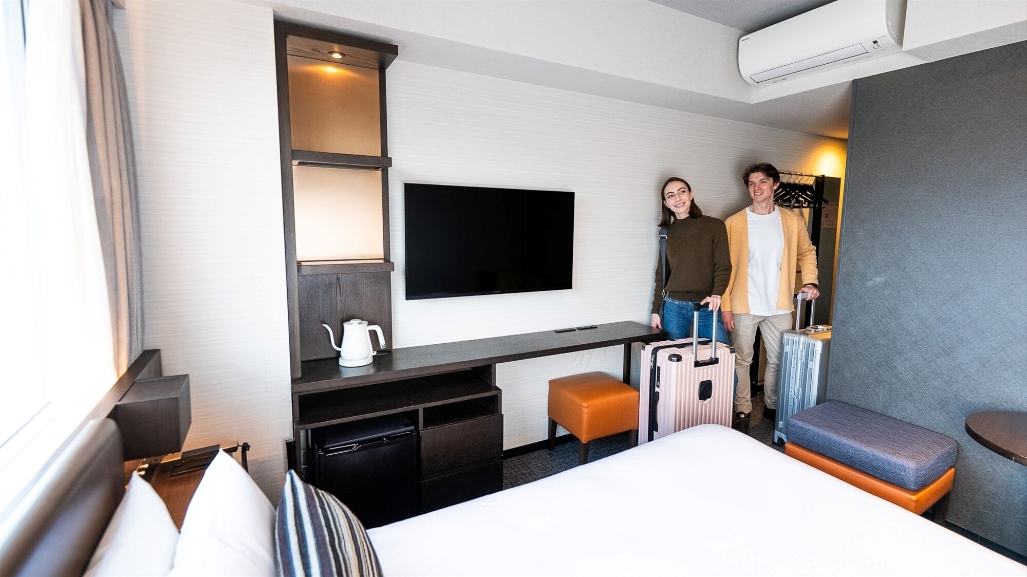 A hotel room with a bed, a desk, a television, a coffee maker, and two suitcases.
