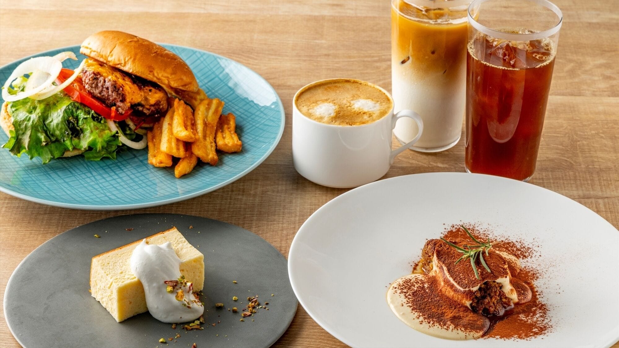 Una comida con hamburguesa, papas fritas, una taza de café, un vaso de té helado y un postre sobre una mesa de madera.