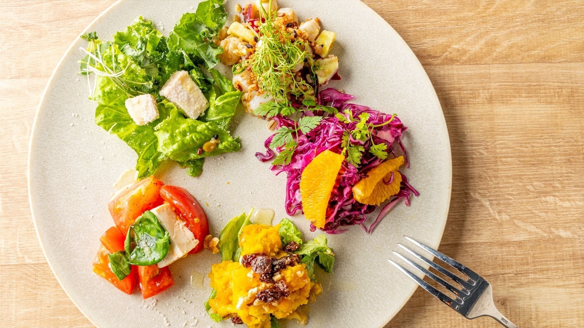 A plate with various salads and a fork on a wooden table.
