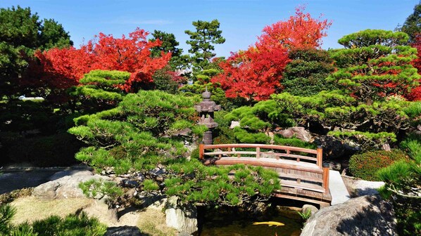 A traditional Japanese garden with a wooden bridge, a stone pagoda, and various trees and shrubs. - Tokyu Stay Hakata (Fukuoka)