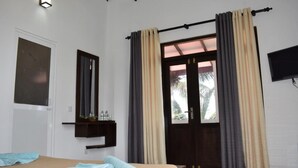 Um quarto com uma cama, uma janela com cortinas, um espelho e uma televisão na parede.
