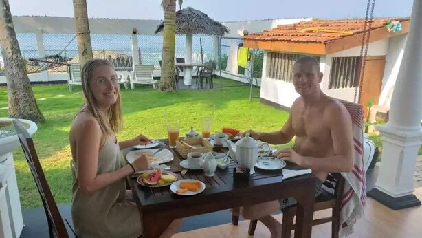 Mesa de jantar com pratos, chávenas e bule, num ambiente exterior soalheiro com vista para o mar.