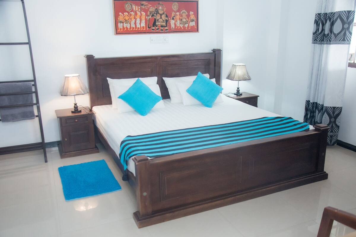 A neatly made bed with a wooden headboard, two bedside tables with lamps, a blue rug, and a wall painting.