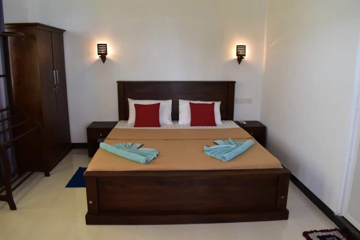 A neatly arranged bedroom with a large bed, two bedside tables, a wardrobe, and wall-mounted lights.