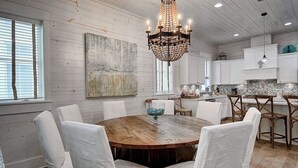 Una cocina rústica con paredes de madera, una mesa de comedor de madera, sillas blancas y un candelabro.