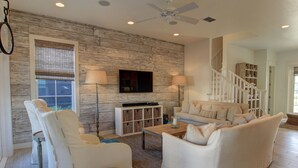 A spacious living room with a modern design, featuring a large sofa, a coffee table, and a television mounted on the wall. - Lakefront Beach Home@Cinnamon Shore North w/ Sunset Views+Amenity Access! (Port Aransas)