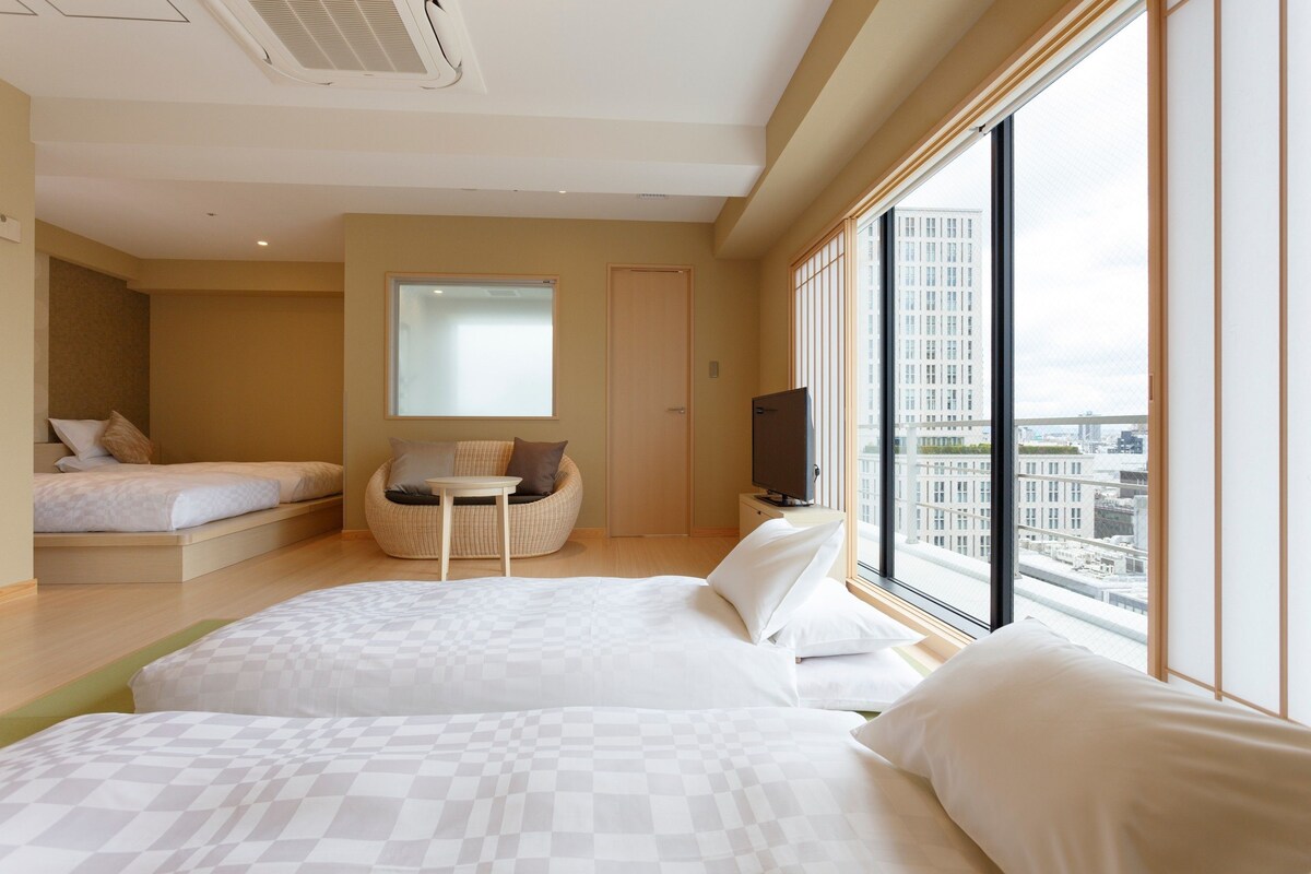A hotel room with two beds, a seating area, a television, and a large window with a city view.
