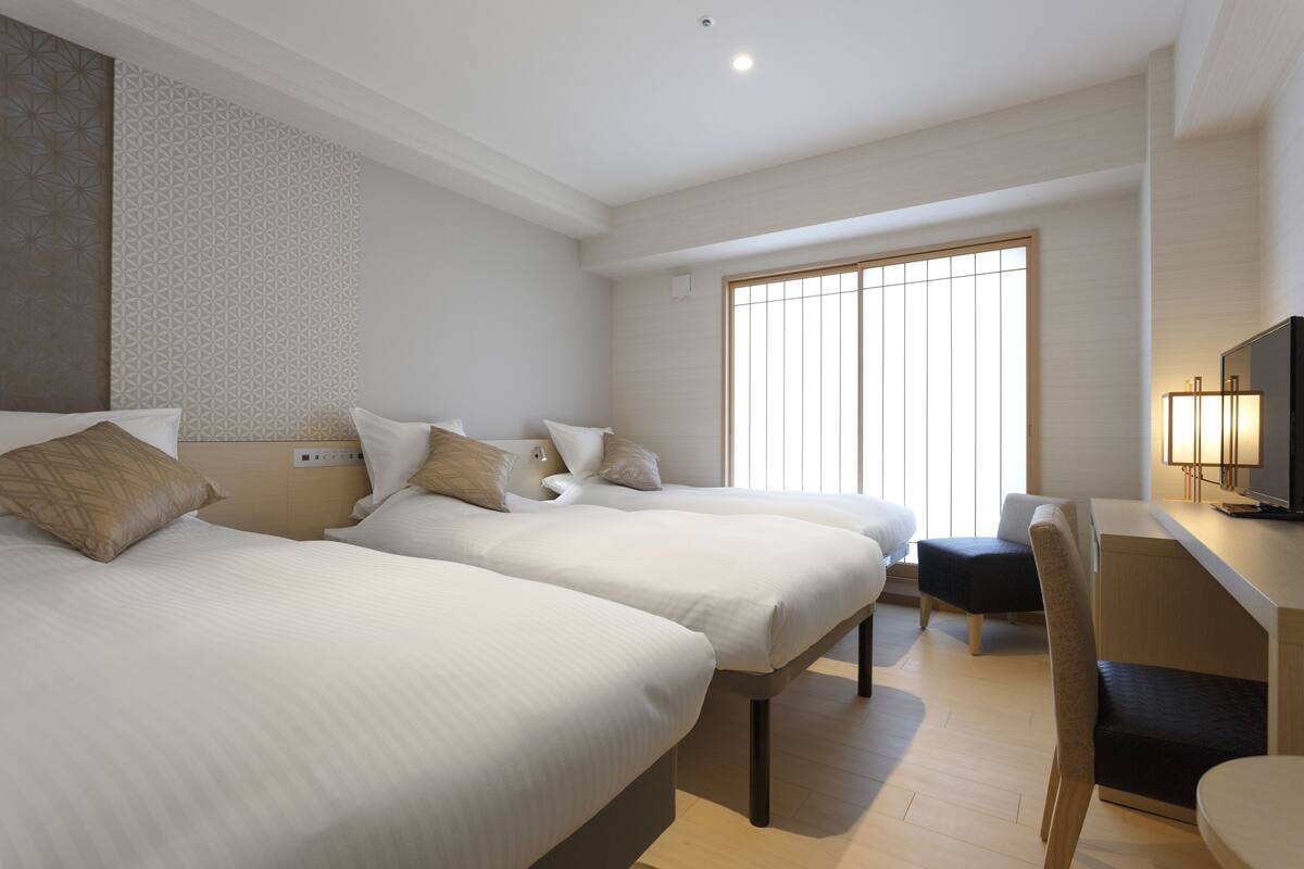 A hotel room with two beds, a desk, a chair, and a TV.