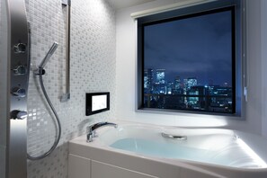 Un baño moderno con bañera, ducha y vistas a la ciudad a través de una ventana.