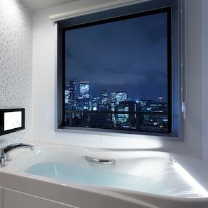 Un baño moderno con una bañera grande, una ventana con vistas a la ciudad y una pared revestida de azulejos.
