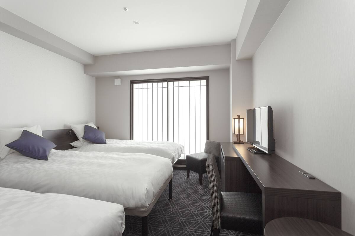 A hotel room with two beds, a desk, a chair, and a television.