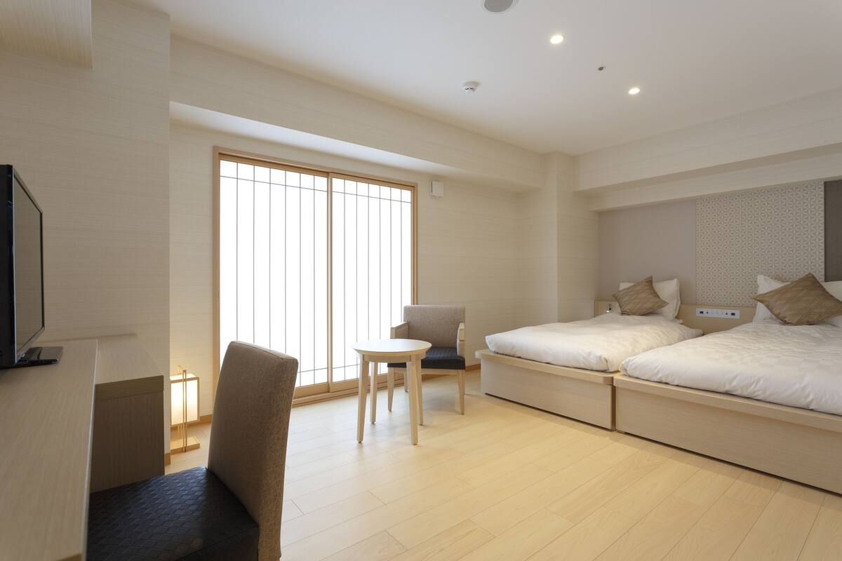 A modern hotel room with a large bed, a desk, a chair, and a TV.