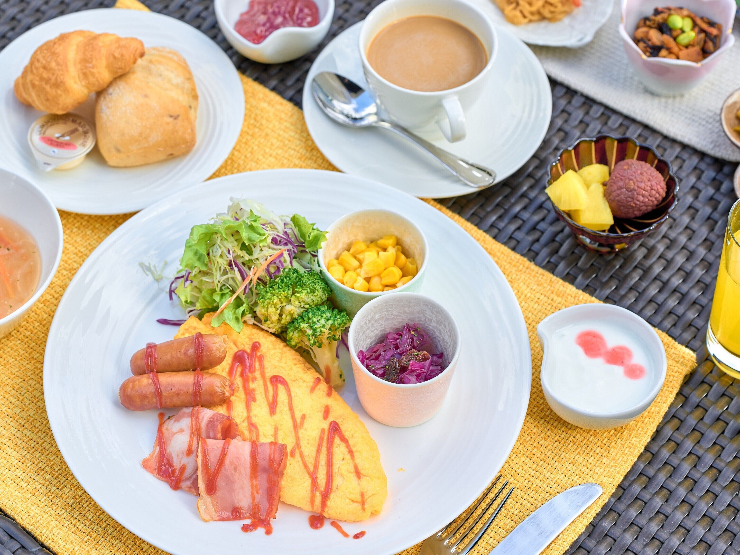 Un desayuno servido en platos con huevos, salchichas y verduras, acompañado de tazas de café y té.