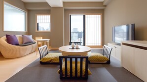 Una sala de estar moderna con un sofá, sillas, una mesa redonda, un televisor y ventanas amplias con vistas a la ciudad.