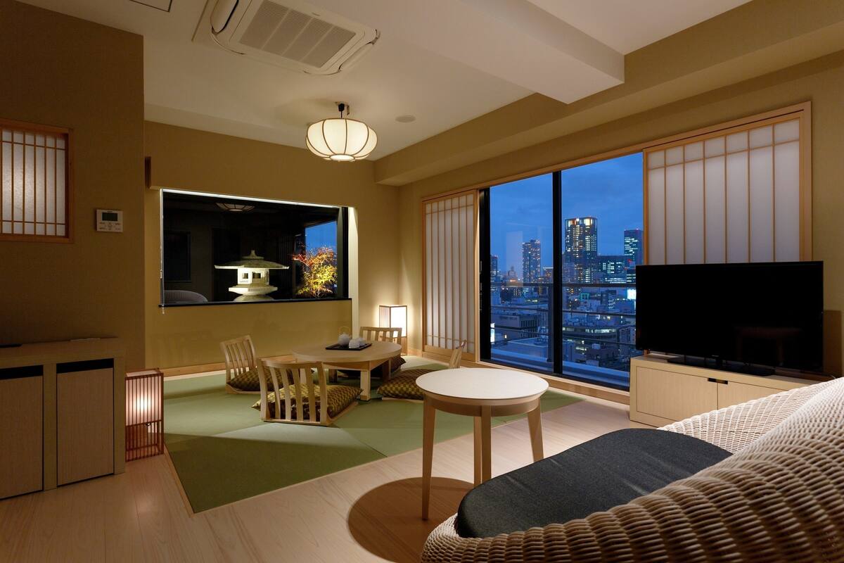 A modern hotel room with a city view, a dining area, and a TV.