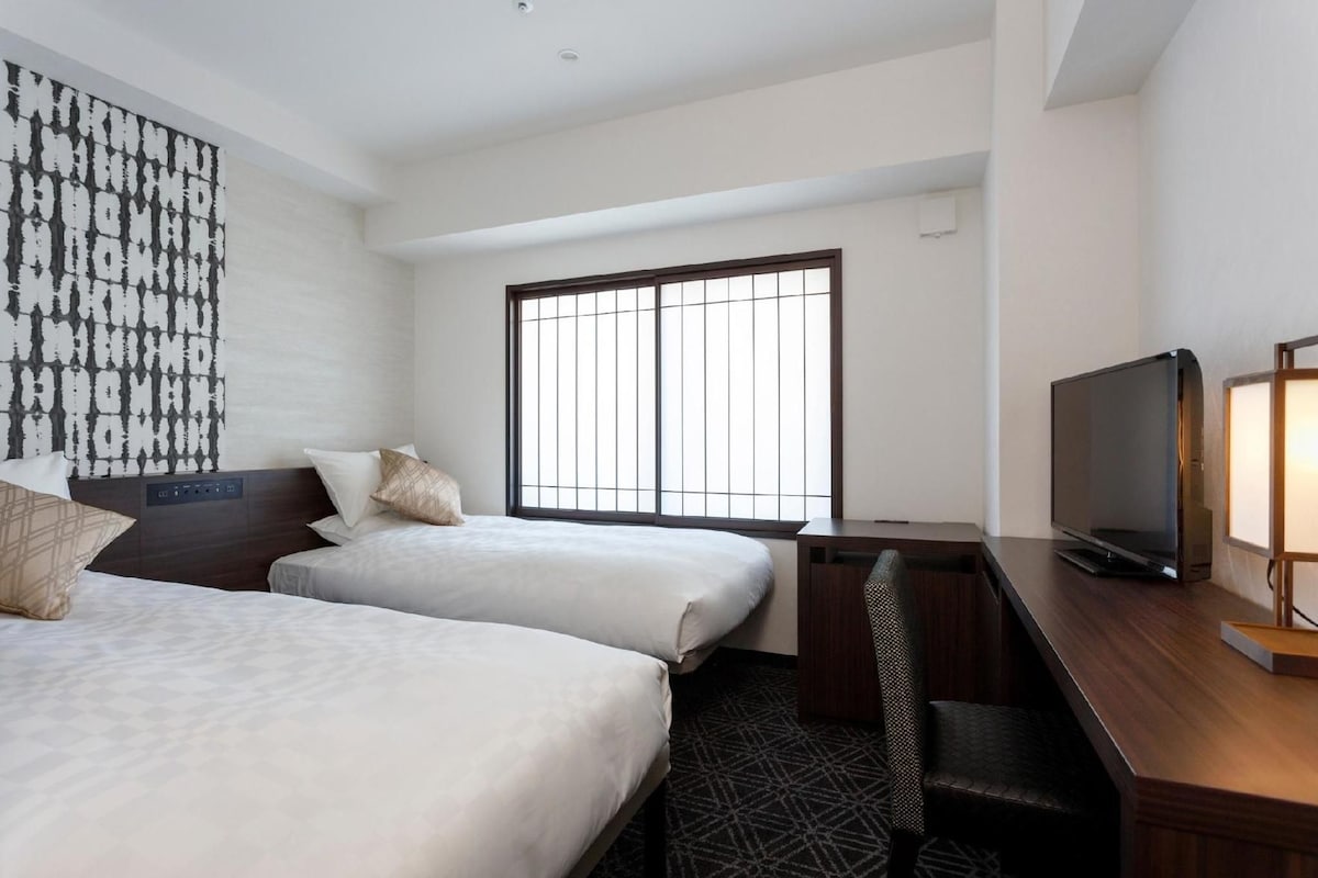A hotel room with two beds, a TV, and a large window with bars.