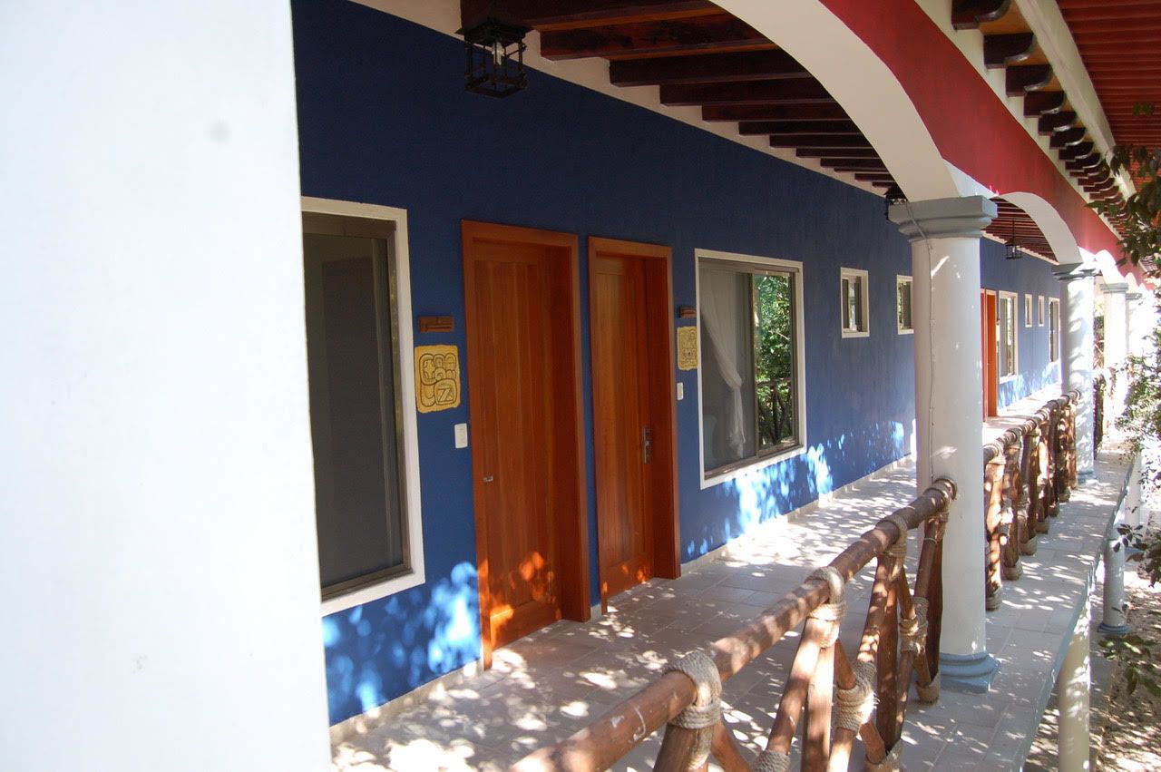 A corridor with wooden doors and windows, a tiled floor, and a wooden railing.