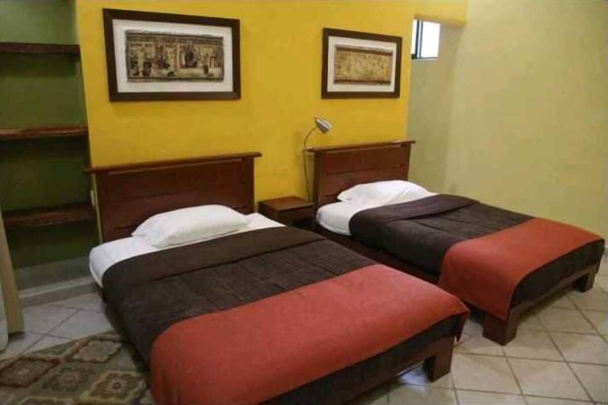 Una habitación con dos camas, una mesita de noche y una lámpara.