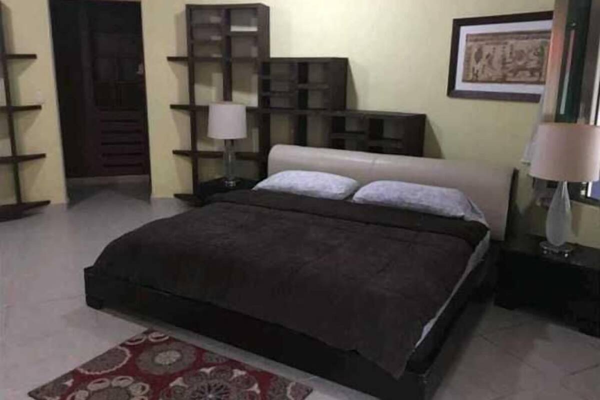 Un dormitorio con cama, mesita de noche, lámpara, estantería y una puerta.