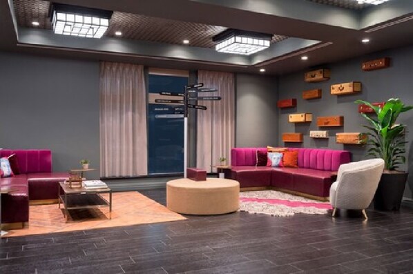A modern living room with a sectional sofa, a round ottoman, and a coffee table. - TRYP by Wyndham Newark Downtown (Newark)