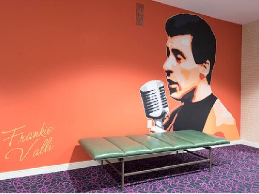 Quarto com um banco verde, um mural na parede e um tapete estampado.