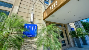 A building entrance with a sign reading "TRYP WYNDAH" and a modern design with a beige facade and palm trees.
