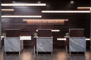 A reception area with a dark wood panel wall and three marble reception desks. - TRYP by Wyndham Newark Downtown (Newark)