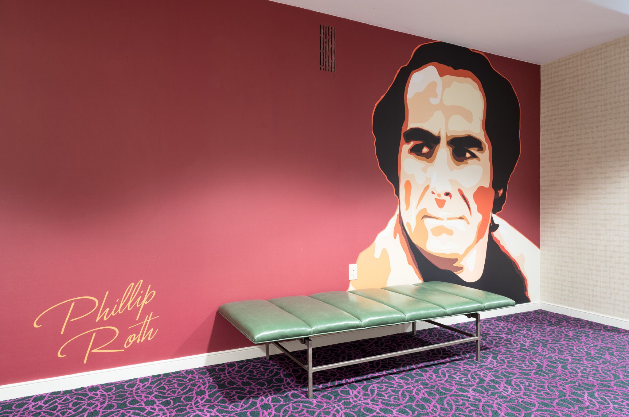 Quarto com um banco verde, uma parede vermelha e um retrato grande.