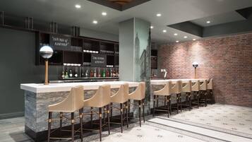 A bar area with a marble countertop, multiple stools, and a brick wall.