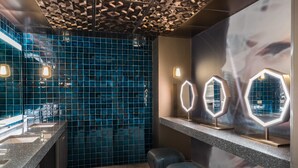 A modern bathroom with a blue tiled wall, a granite countertop, and a mirror with illuminated edges.
