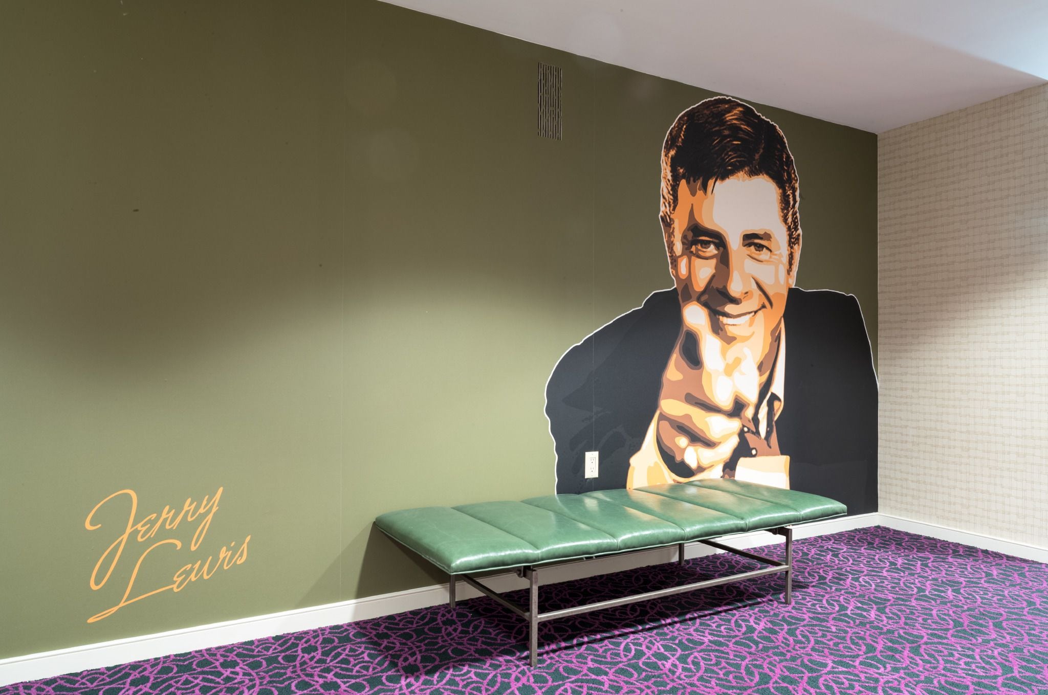 Una habitación con una pared verde, un retrato grande y un banco verde.
