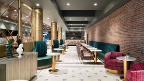 A modern restaurant interior with a brick wall, green seating, and gold accents.