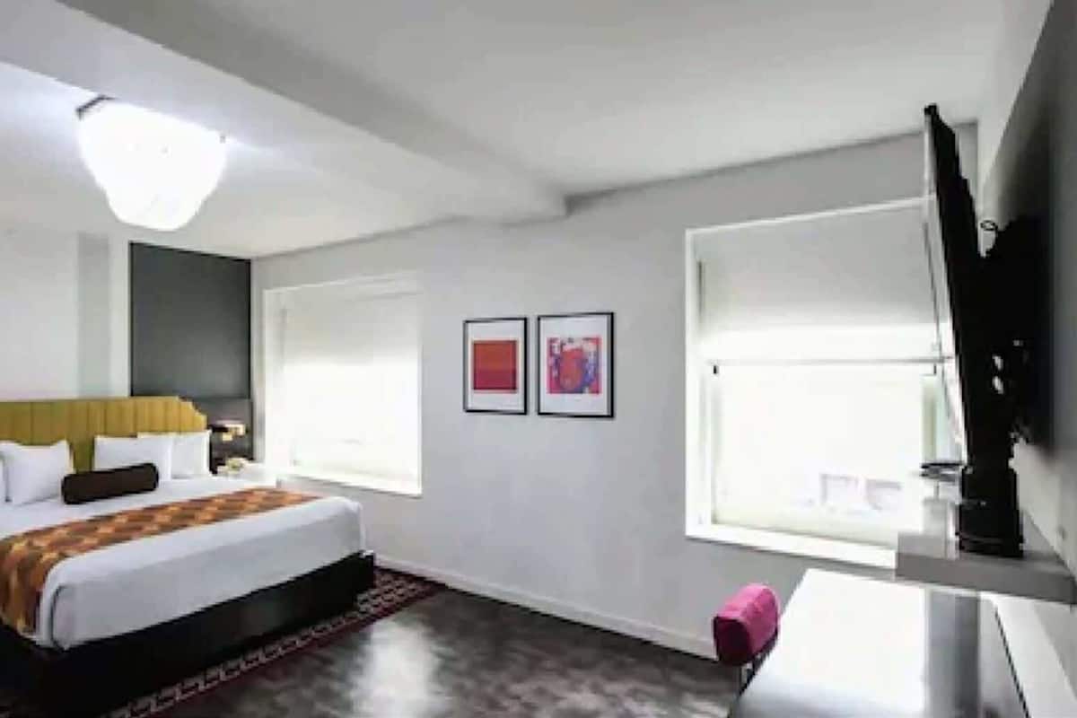 Une chambre d’hôtel moderne équipée d’un lit, de tables de chevet, d’un bureau, d’une chaise et d’un téléviseur fixé au mur.