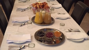A dining table set for breakfast with croissants, juice, and jams.
