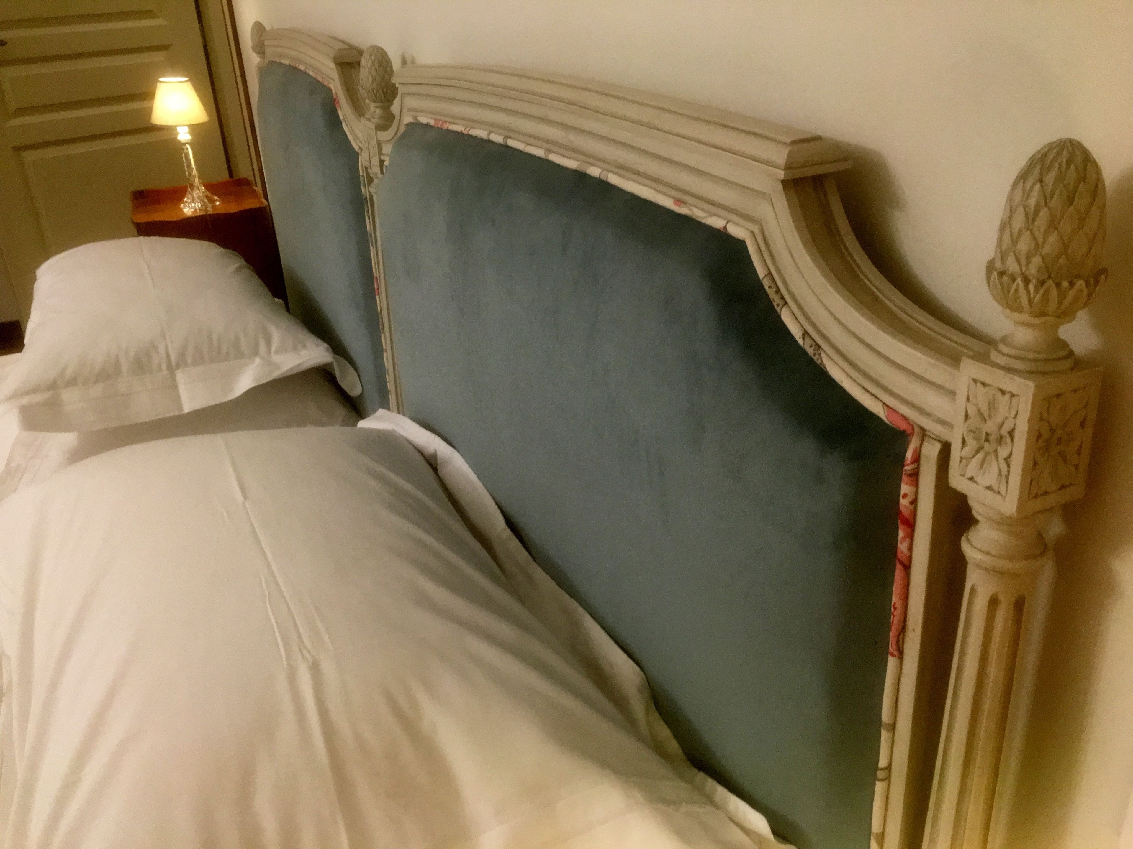 A bed with a white comforter and pillows, a nightstand with a lamp, and a decorative headboard.