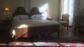A bedroom with a large bed, two bedside lamps, a chair, and a window with curtains.
