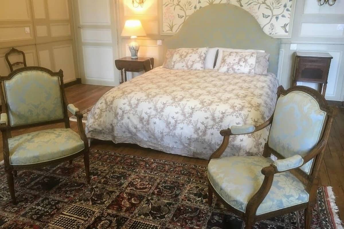 Un dormitorio tradicional con una cama grande, dos sillones tapizados, un suelo con estampado y papel tapiz floral.