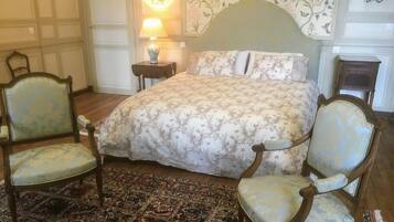 Una camera da letto tradizionale con un letto grande, due poltrone imbottite, un tappeto decorato e carta da parati floreale.