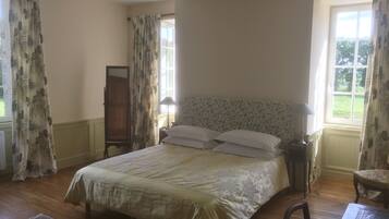 A bedroom with a large bed, a nightstand with a lamp, a wooden wardrobe, and a window with curtains.