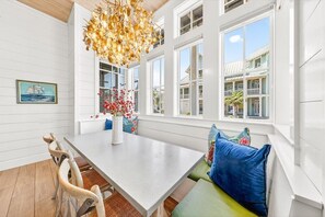 A dining area with a table, chairs, and a bench with cushions. There is a window with a view of buildings outside. - Beach Home w/ Screen Porch near Beach Boardwalk, Pool+More Great Amenities (Port Aransas)