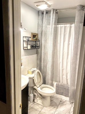 A bathroom with a toilet, sink, and shower curtain. - The Cottages of Lynchburg (Lynchburg)