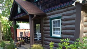 A log cabin with a porch, outdoor seating, and a landscaped garden with various plants and rocks.