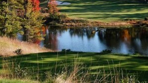 A golf course with a pond, surrounded by trees with autumn foliage.