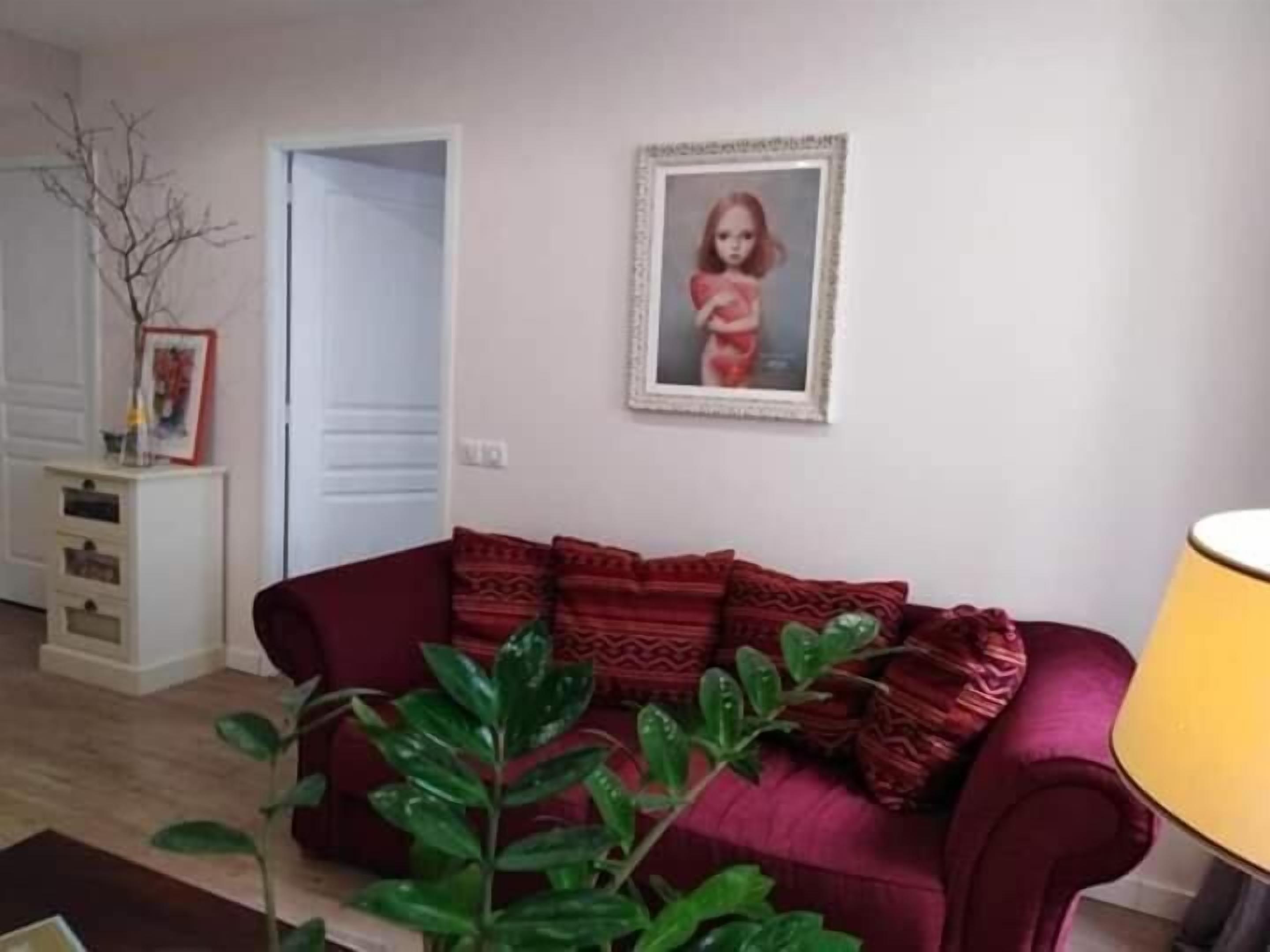 Una sala de estar con un sofá rojo, una planta y un cuadro en la pared.