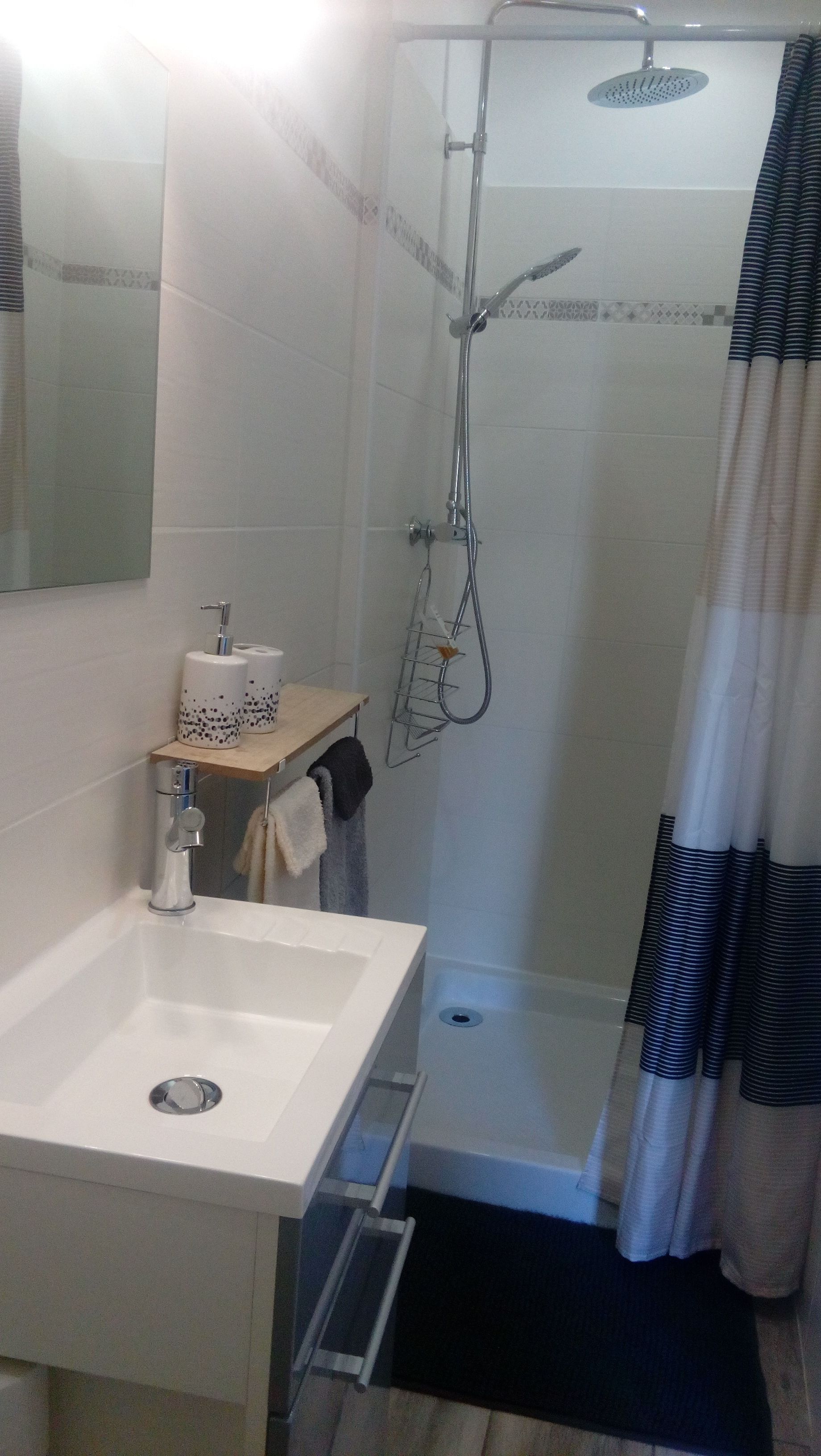 Een badkamer met een wit wastafel, een spiegel, een douche met handdouche en een handdoekhouder.