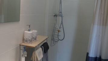Een badkamer met een wit wastafel, een spiegel, een douche met handdouche en een handdoekhouder.