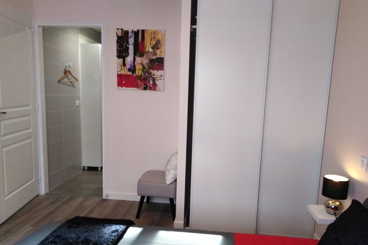 Un dormitorio con cama, una mesita de noche con lámpara, un taburete pequeño y un cuadro abstracto y colorido en la pared.